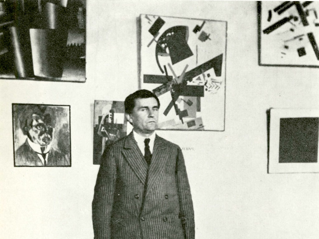 Abstract artist Kazimir Malevich standing in front of his paintings, circa 1924.